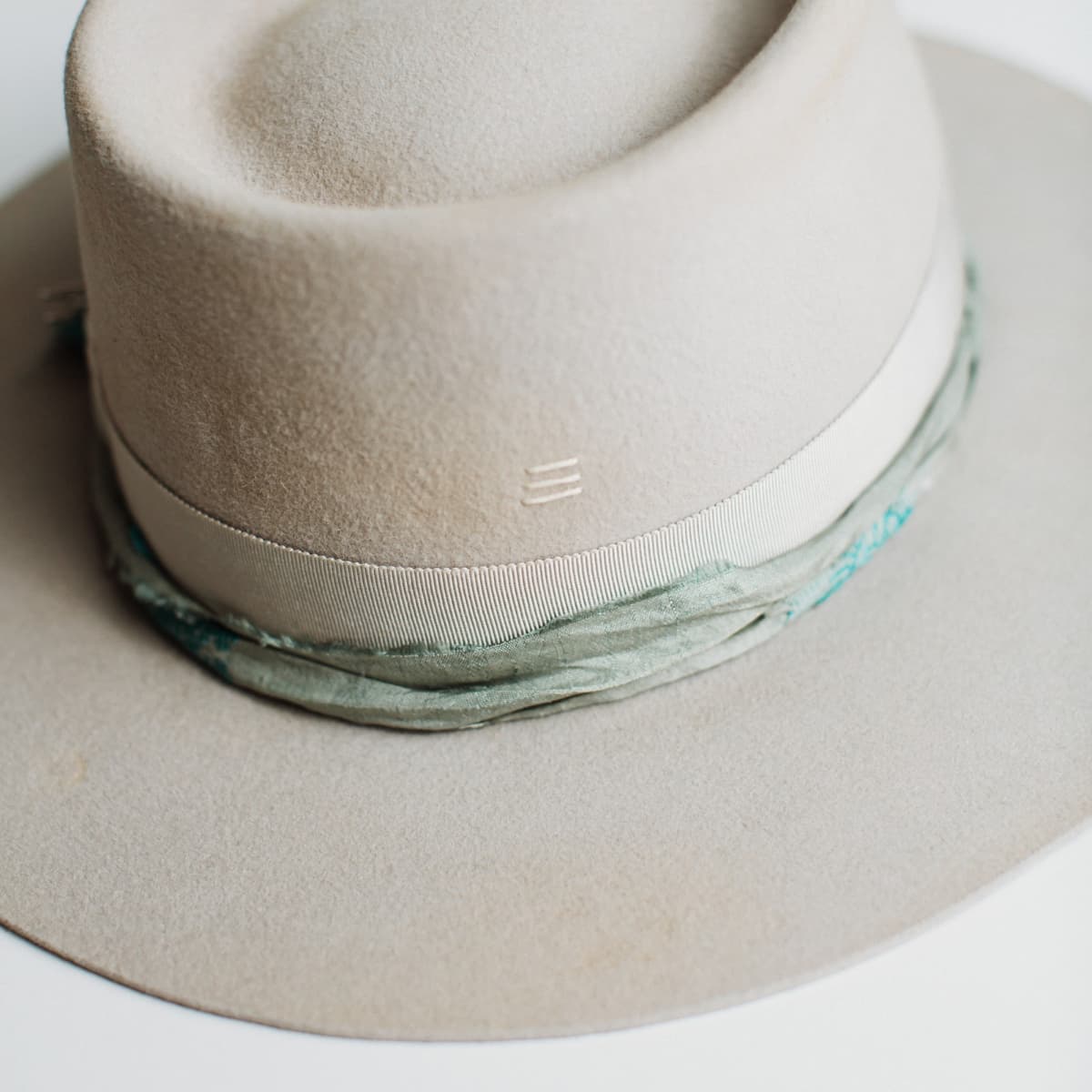 Close-up detail of The Dove felt hat showing blue and teal sari silk trim, silver hat pin and ivory beaded charm by PHYLLi Designs.