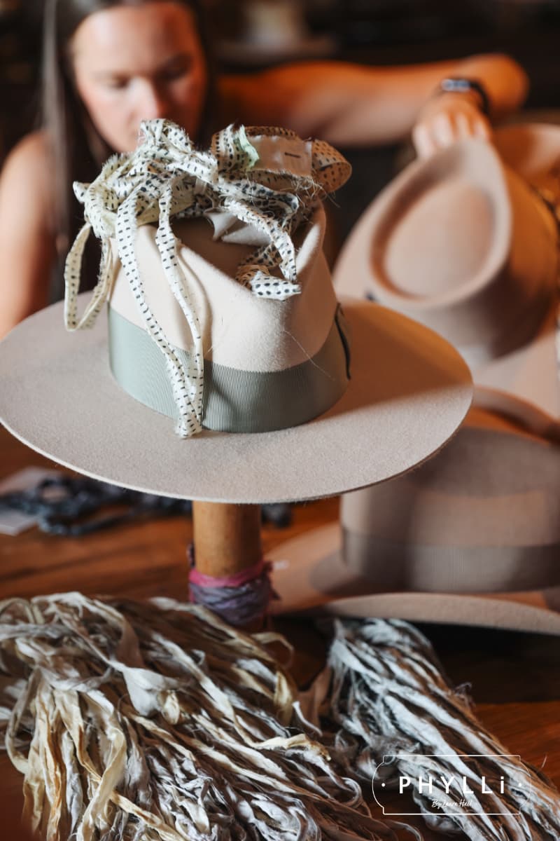 Custom felt hat styled with silk ribbon and trims on a hat stand during the PHYLLi Group Hat Party experience.