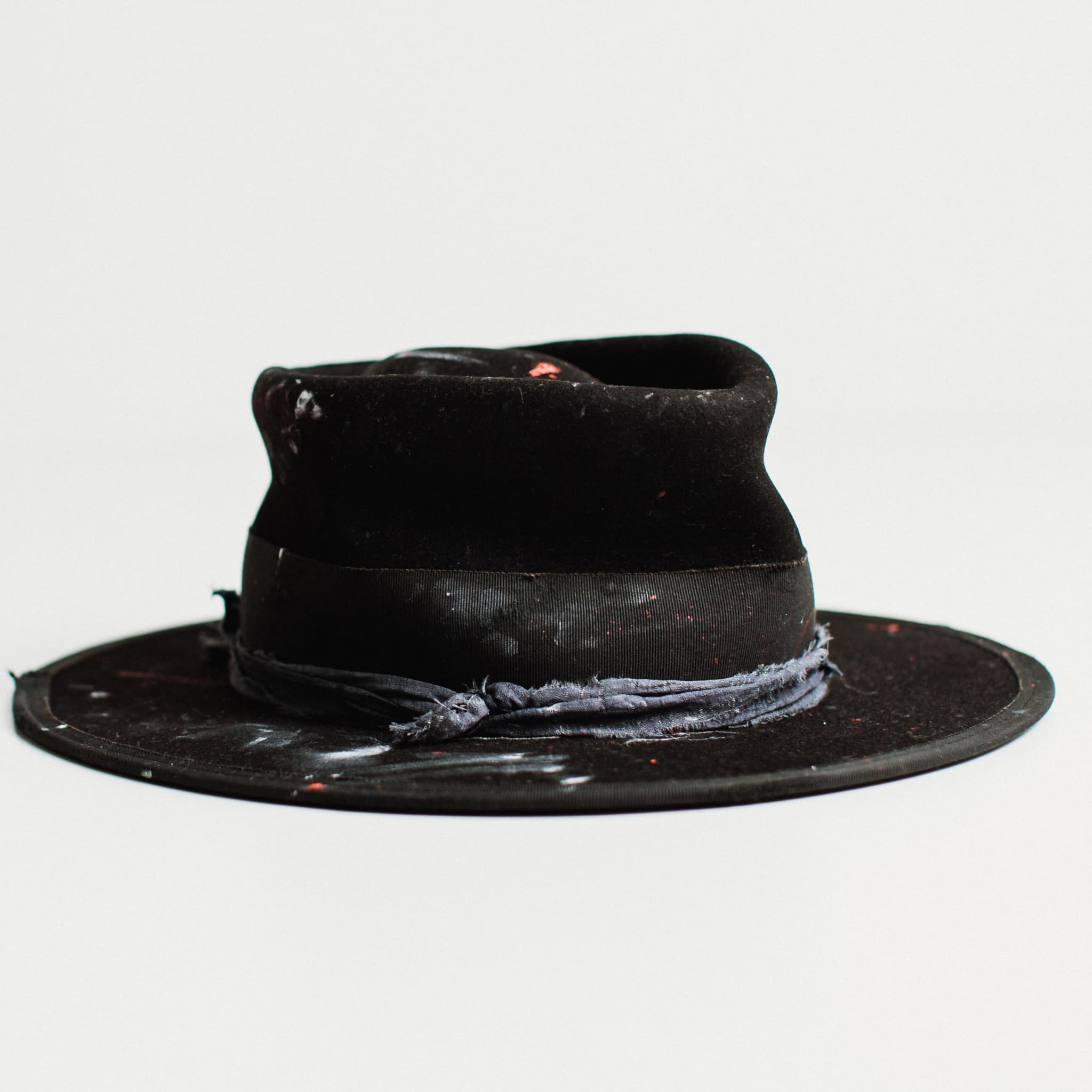 Front right angled view of black felt hat with medium brim and paint-speckled decorative band by PHYLLi Designs.