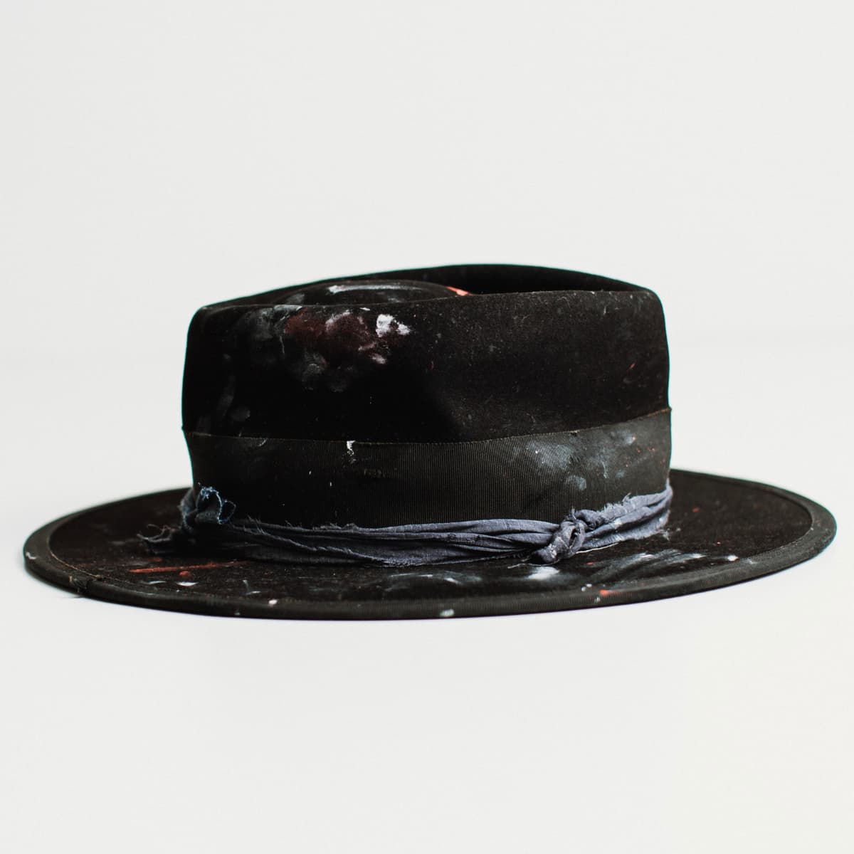 Right side view of black felt hat with medium brim and paint-speckled decorative band on a white background.