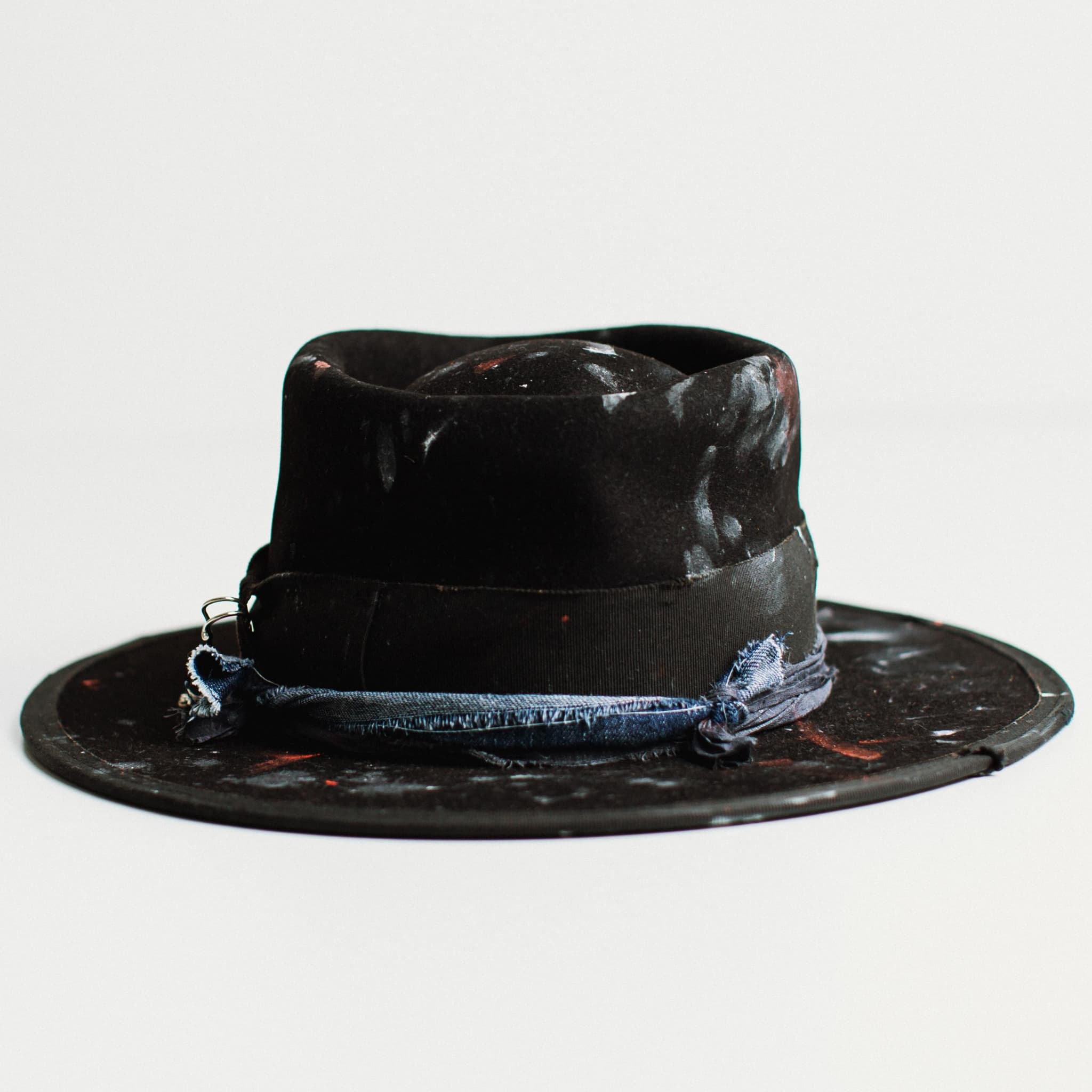Back view of black felt hat with medium brim and paint-speckled decorative band on a white background.