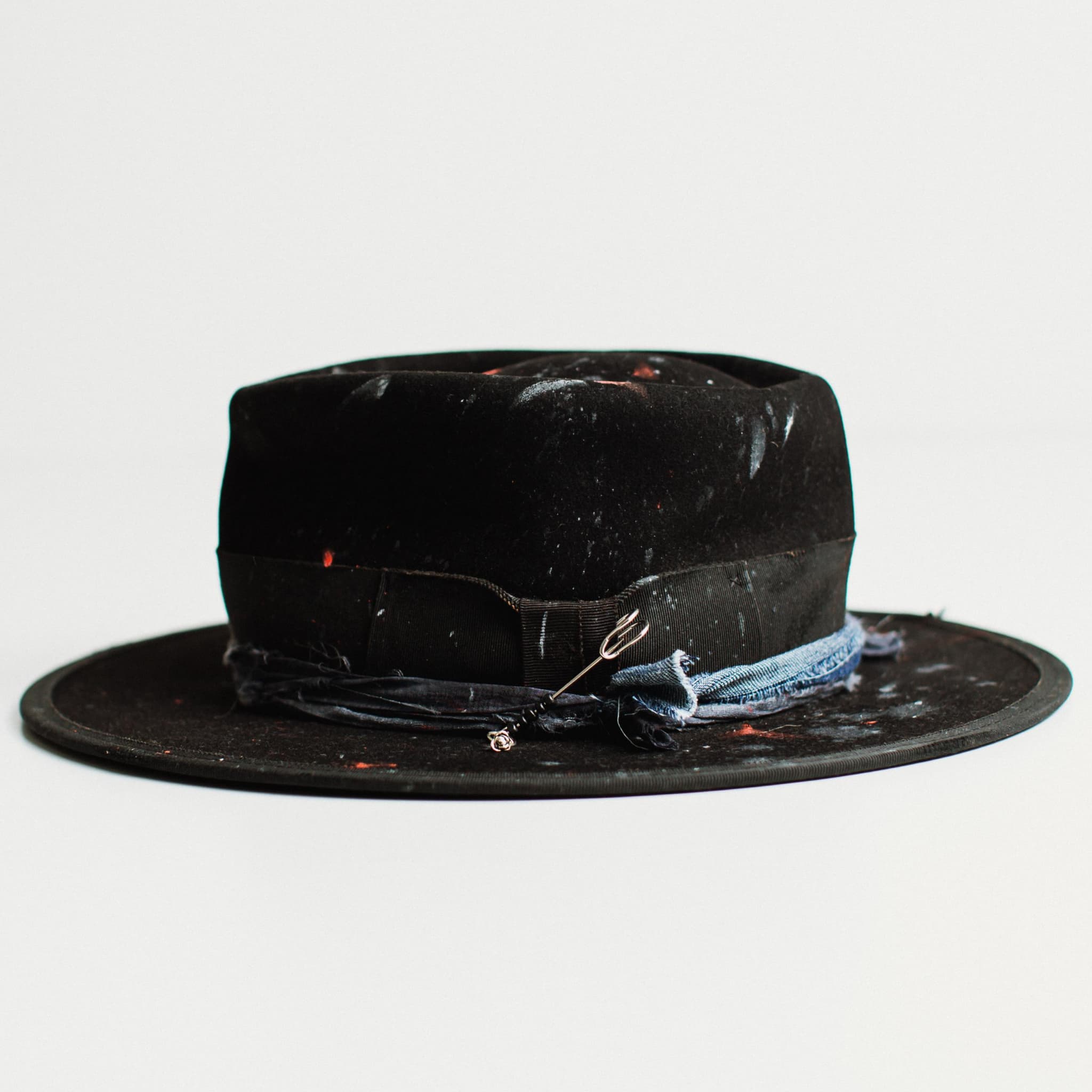 Left side view of black felt hat with medium brim and paint-speckled decorative band by PHYLLi Designs on a white background.