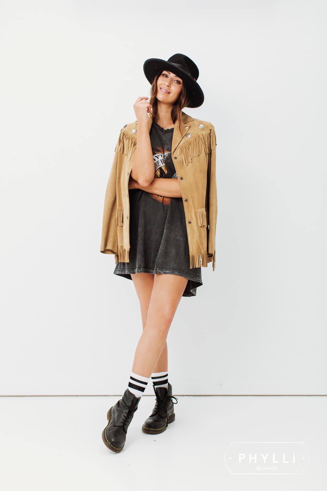 Woman wearing a black felt hat by PHYLLi Designs styled with a tan fringe jacket and black dress.