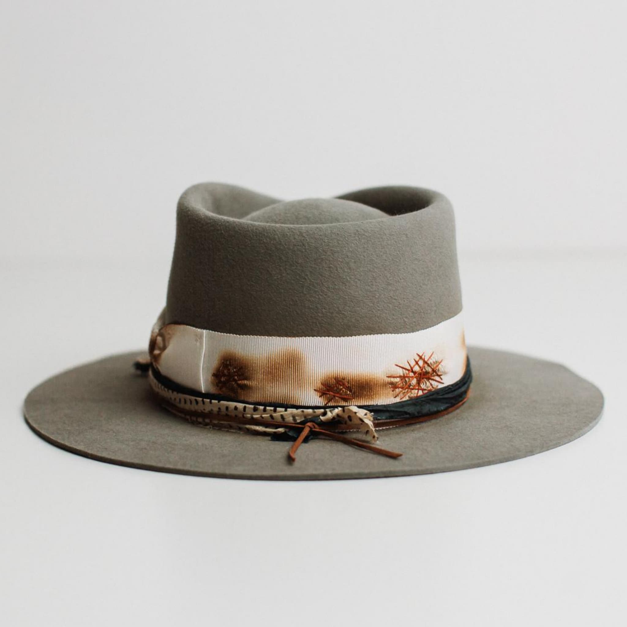 Back view of The Paver taupe felt hat by PHYLLi Designs featuring distressed ivory grosgrain band and rust darned patches.