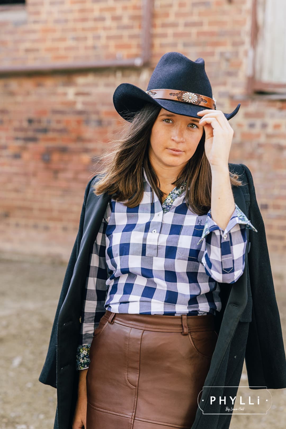 Model wearing The PHYLLi dark navy felt hat by PHYLLi Designs with Buffalo Girl Rugged Desert tie back band in front of a heritage brick building.