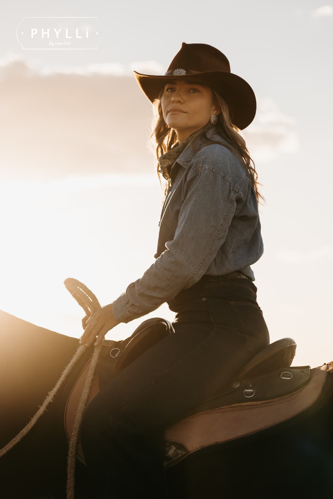 Cowgirl wearing the Caramel cowboy hat The PHYLLi Caramel by PHYLLi Designs with Buffalo Girl Western floral tie back hat band on horseback during golden hour.