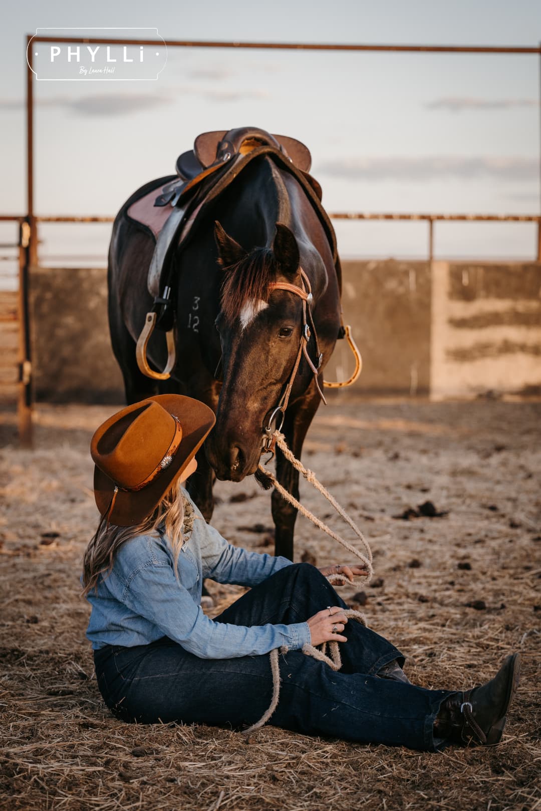 Cowgirl wearing the Caramel cowboy hat The PHYLLi Caramel by PHYLLi Designs with Buffalo Girl Western floral tie back hat band while interacting with a horse in a rustic paddock setting.