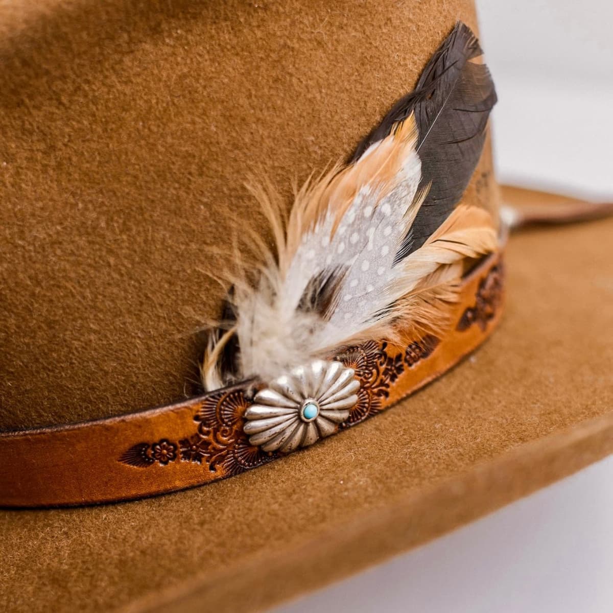 Close up detail of the The PHYLLi Caramel cowboy hat showing floral tooled leather band with feather detail.