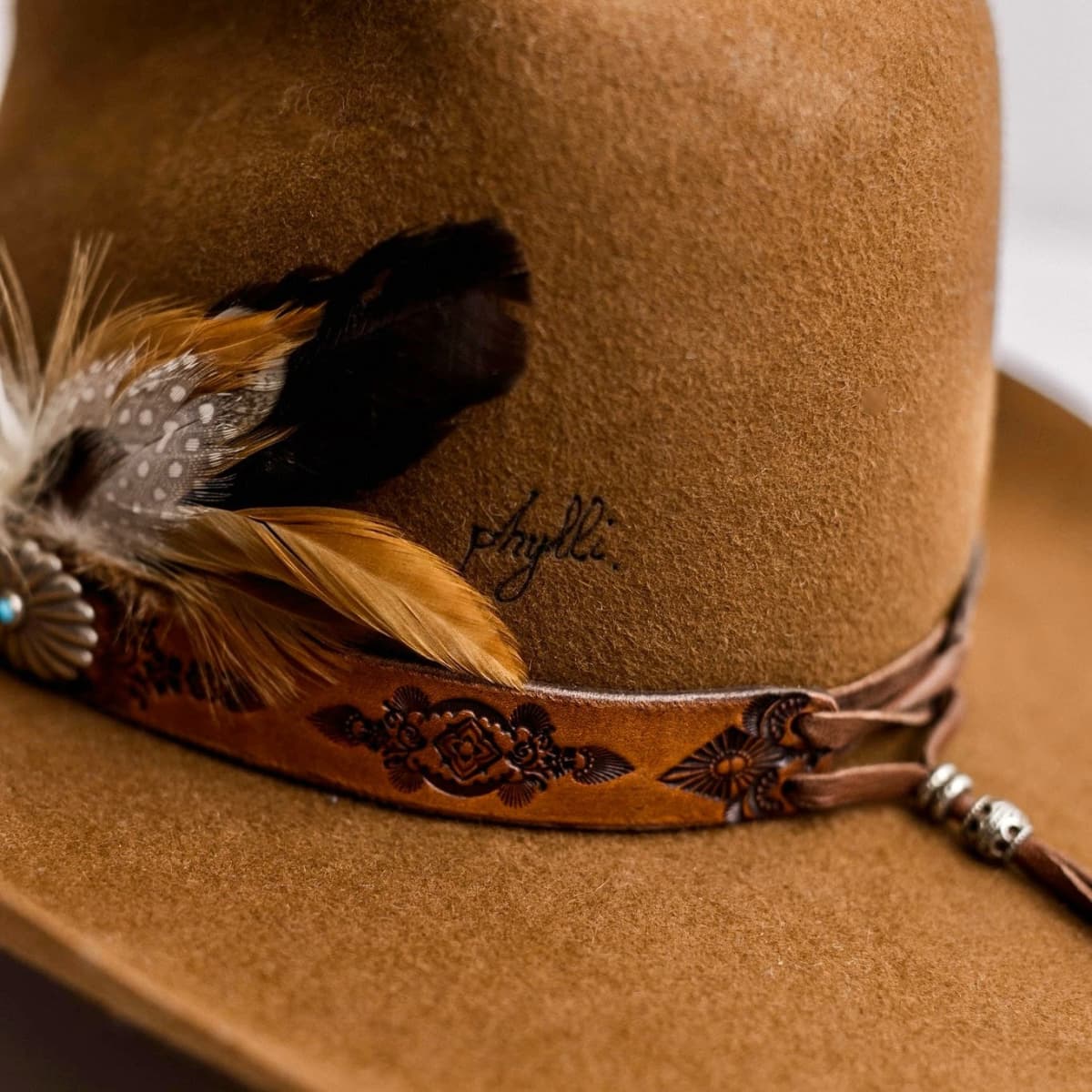 Close up detail of the The PHYLLi Caramel cowboy hat showing Buffalo Girl Western floral tie back hat band with assorted fallen feather bunch.