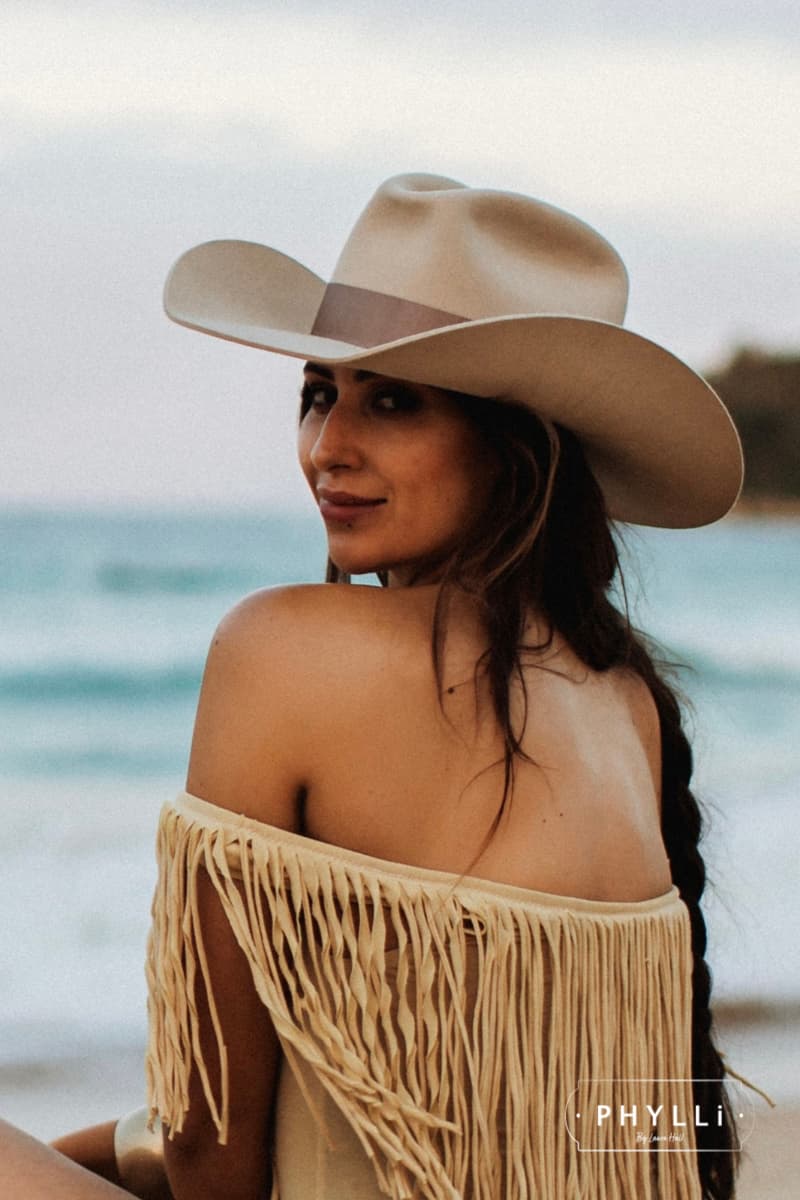 Beach lifestyle image of woman wearing The Plains beige rabbit felt cowboy hat with wide shaped brim by PHYLLi Designs.
