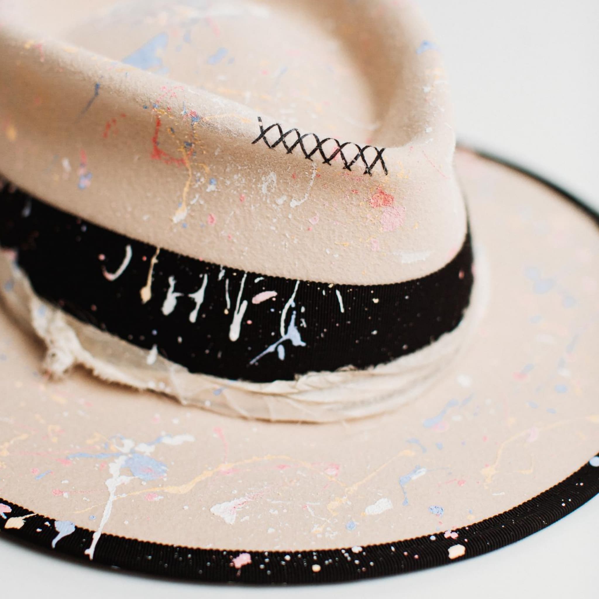 Close-up detail of Pollock beige felt hat by PHYLLi Designs showing paint splatter finish and hand-stitched crosses.