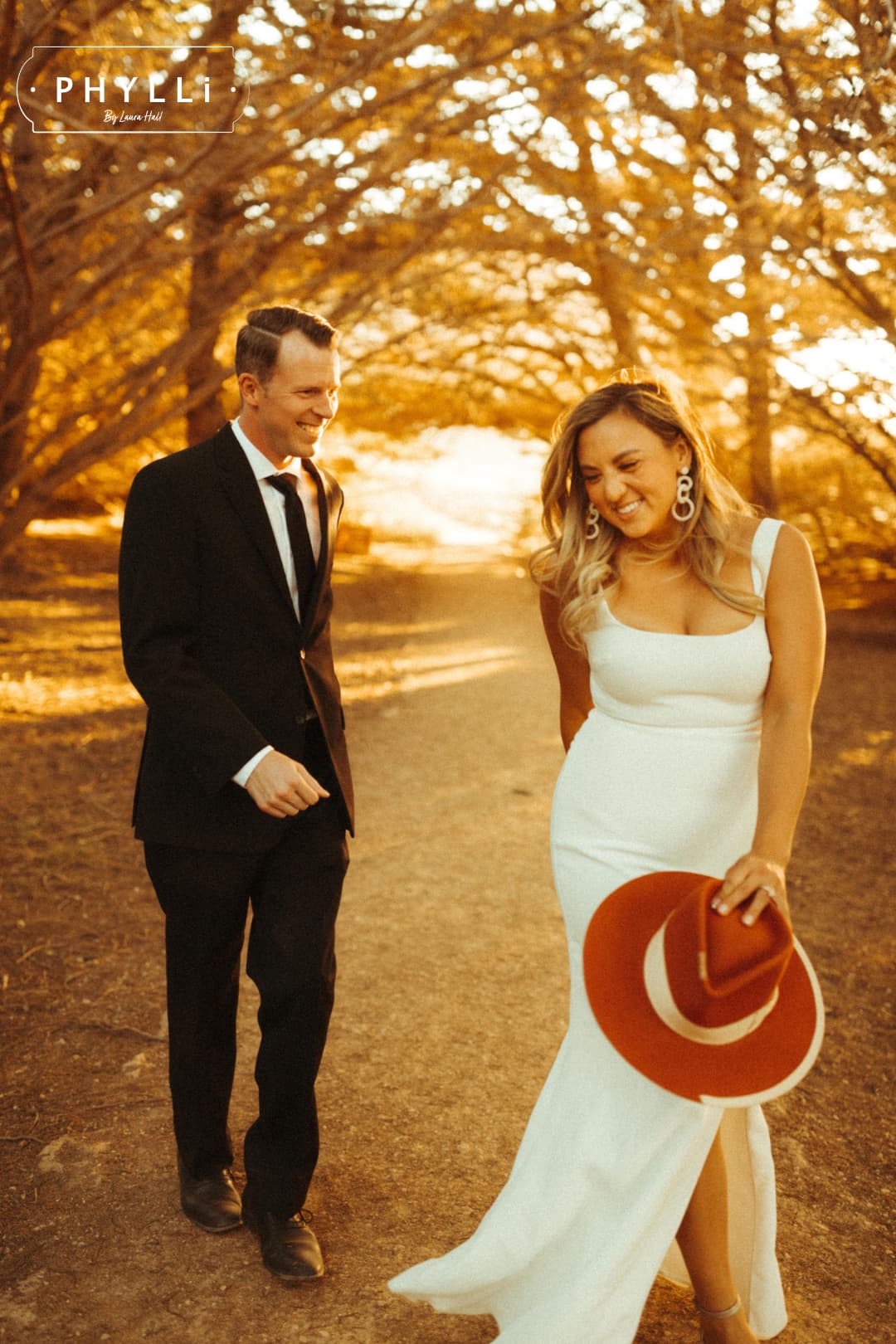 Bride and groom walking through a park with the bride holding her spiced pumpkin Producer felt hat.
