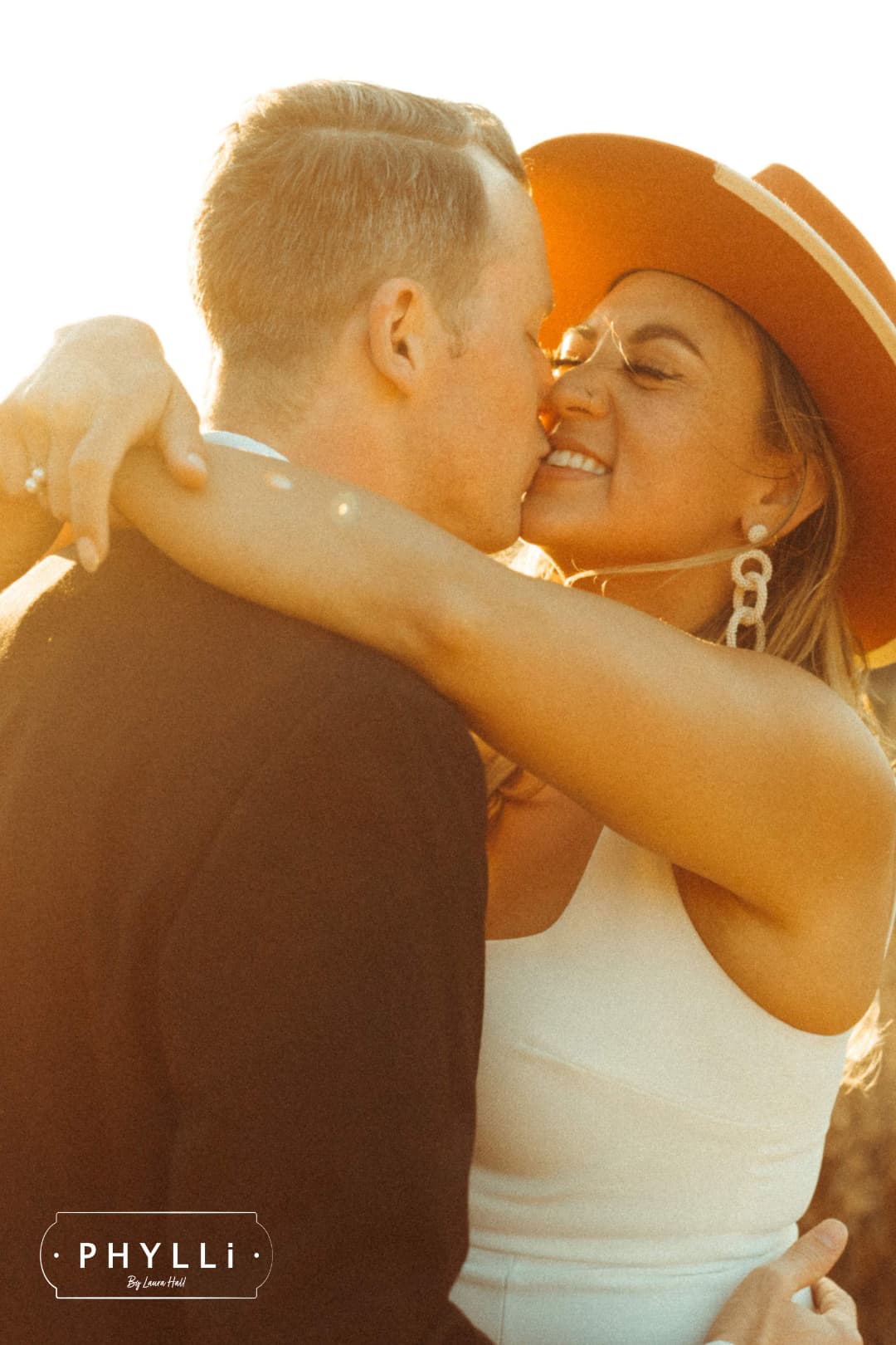 Bride wearing a spiced pumpkin Producer felt hat embracing her partner outdoors.