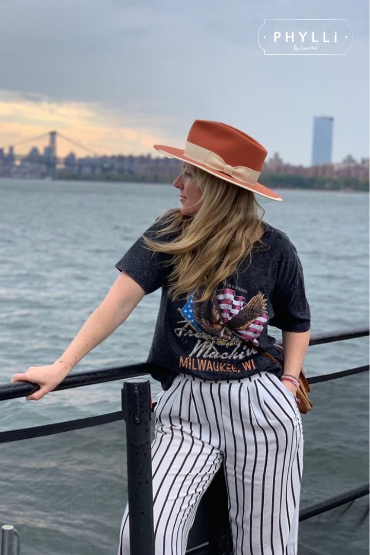 Woman wearing the spiced pumpkin Producer felt hat styled with a graphic tee and striped pants by the waterfront.