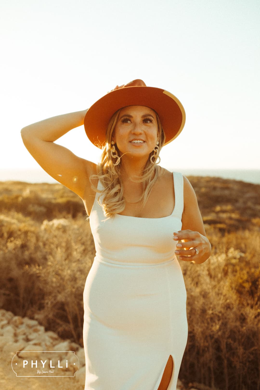 Bride wearing the spiced pumpkin Producer felt hat with a wedding dress in a field.