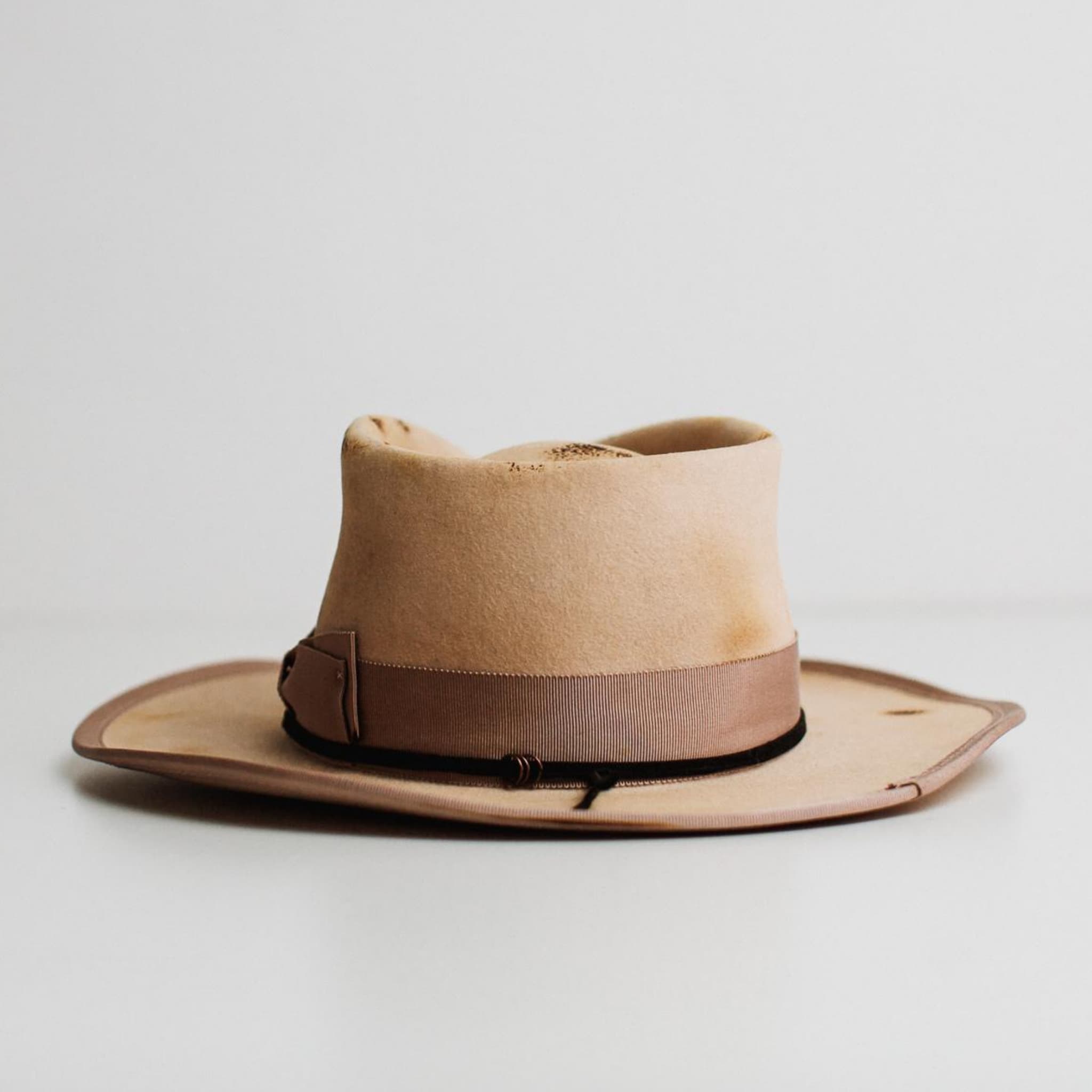 Back view of Ringleader beige distressed felt hat by PHYLLi Designs showing plaster grosgrain double bow band and black suede string detail.