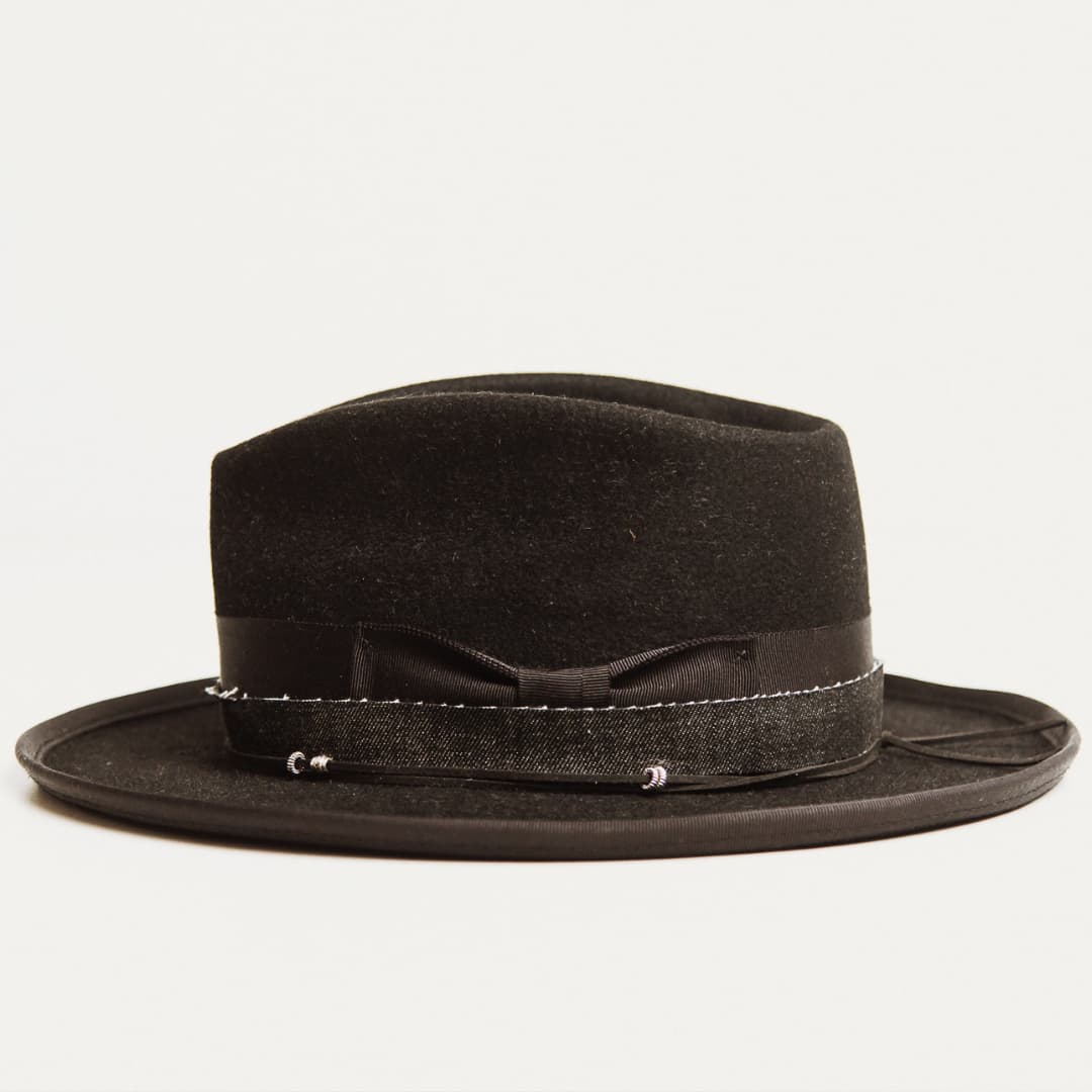 Side view of black felt hat with decorative band and pencil curl brim on a light grey background.