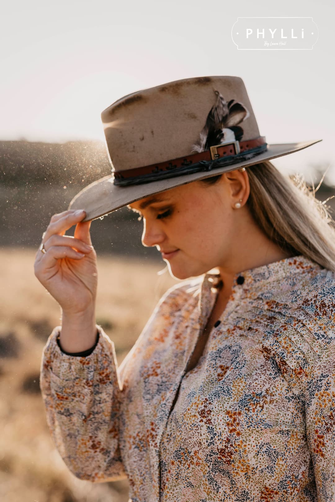 Laura Hall, founder of PHYLLi Designs, wearing The Safari distressed Sahara felt hat with feather detail in golden hour countryside.