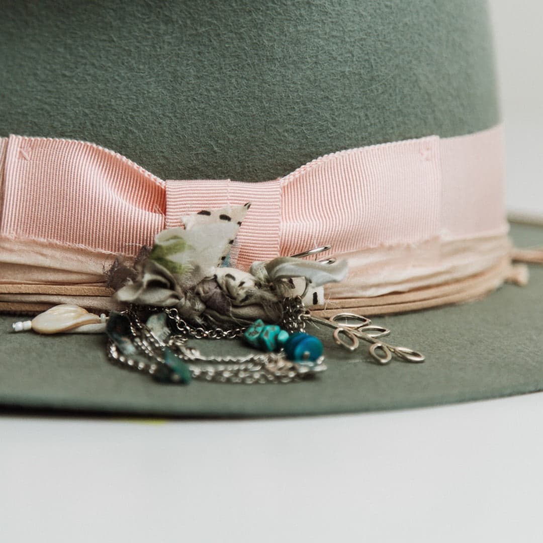 Close up detail of The Sage felt hat showing sherbet pink grosgrain bow band and silver chunky hat pin with sari silks, tassel, charms and beads.