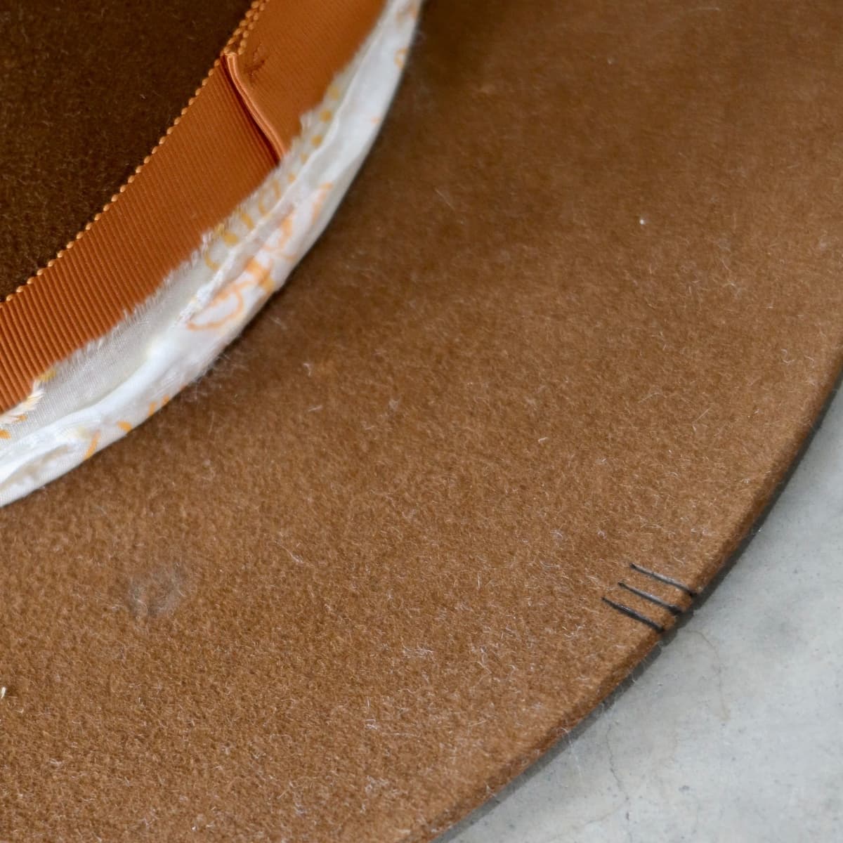 Close-up of caramel felt hat brim showing branded line markings and felt texture by PHYLLi Designs.
