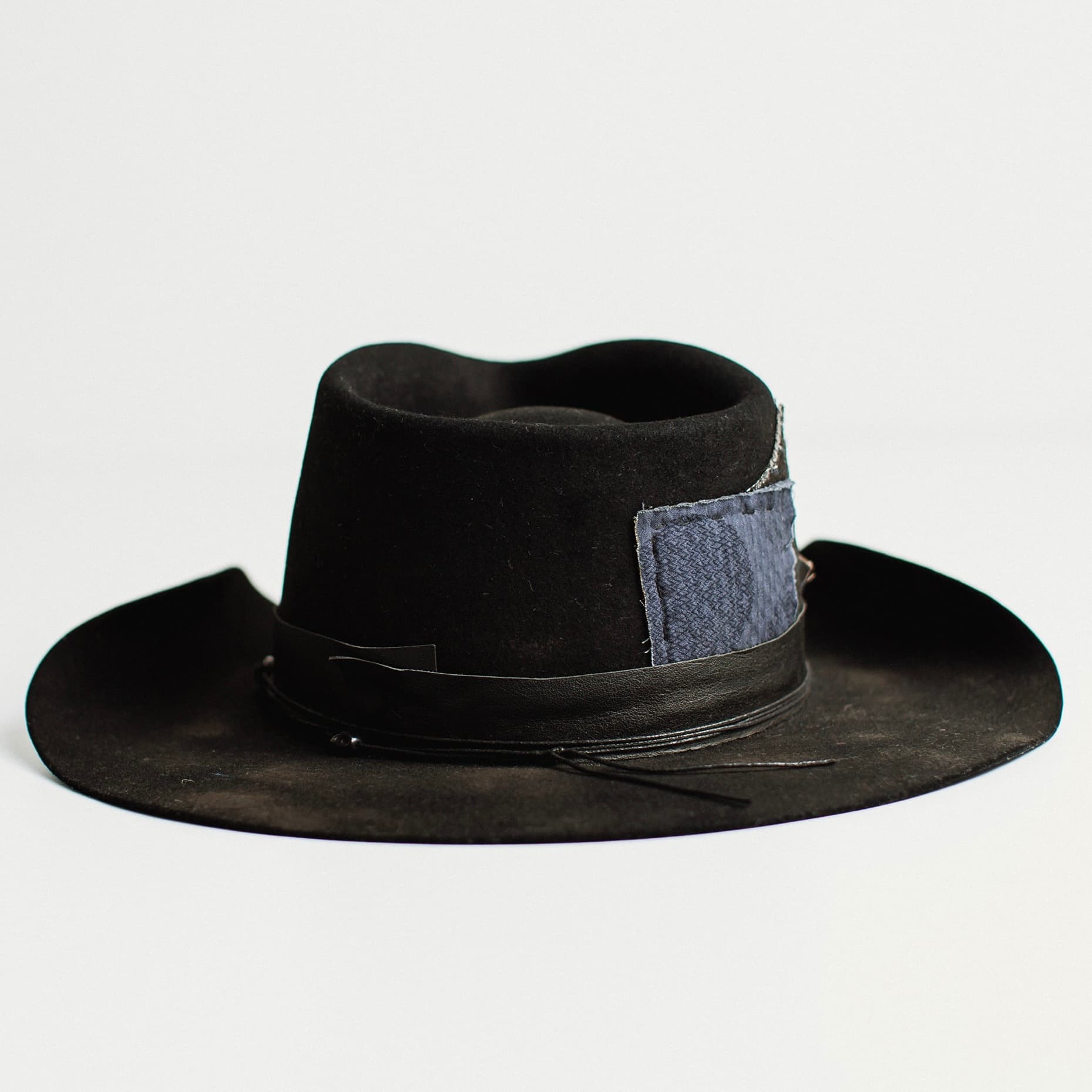 Back view of black felt cowboy hat with denim patch detail by PHYLLi Designs on a white background.