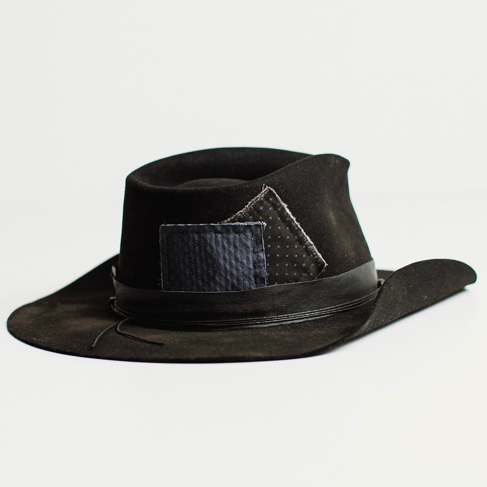 Back angled view of black felt cowboy hat with denim patches and leather band by PHYLLi Designs.