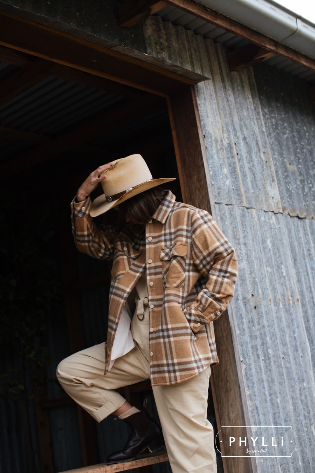 Woman standing in barn doorway wearing The Wheeler premium felt hat in distressed Beige.
