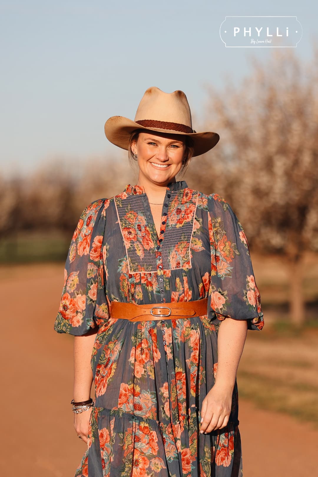 Laura Hall standing in orchard wearing The Wheeler premium felt hat in distressed Beige with 12 strand leather hat band in Chocolate.