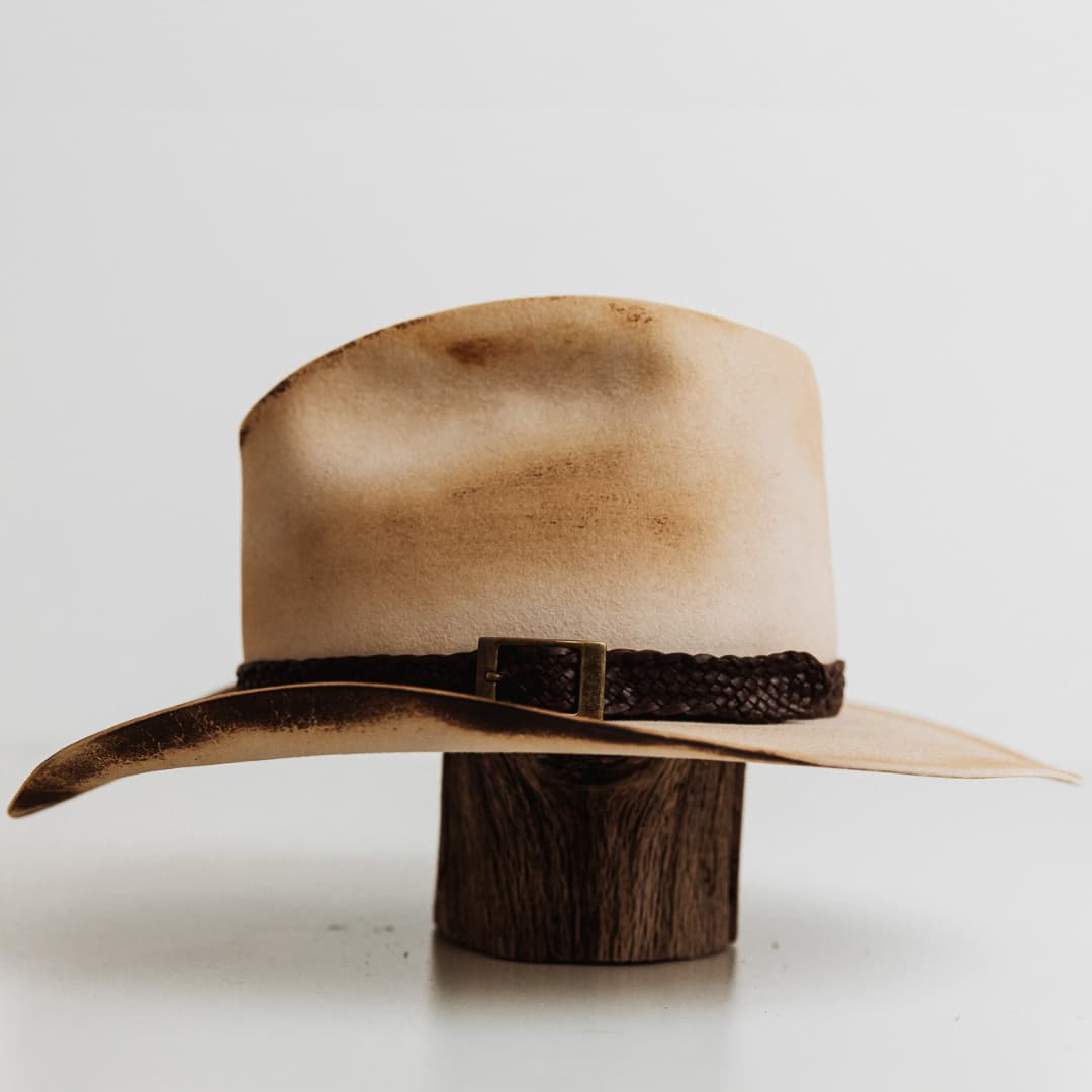 Left side view of The Wheeler premium felt hat in distressed Beige with 12 strand leather hat band in Chocolate.