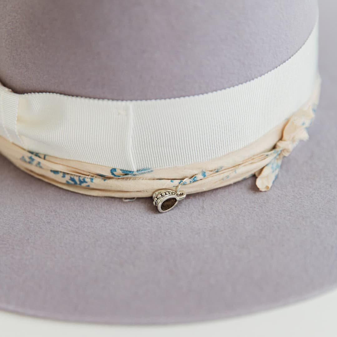 Close up of patterned charm detail, sari silk trim and ivory grosgrain band on The Wisteria felt hat by PHYLLi Designs.