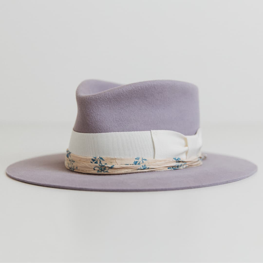 Front left angle of The Wisteria lilac felt hat by PHYLLi Designs featuring ivory grosgrain bow band and patterned sari silk.