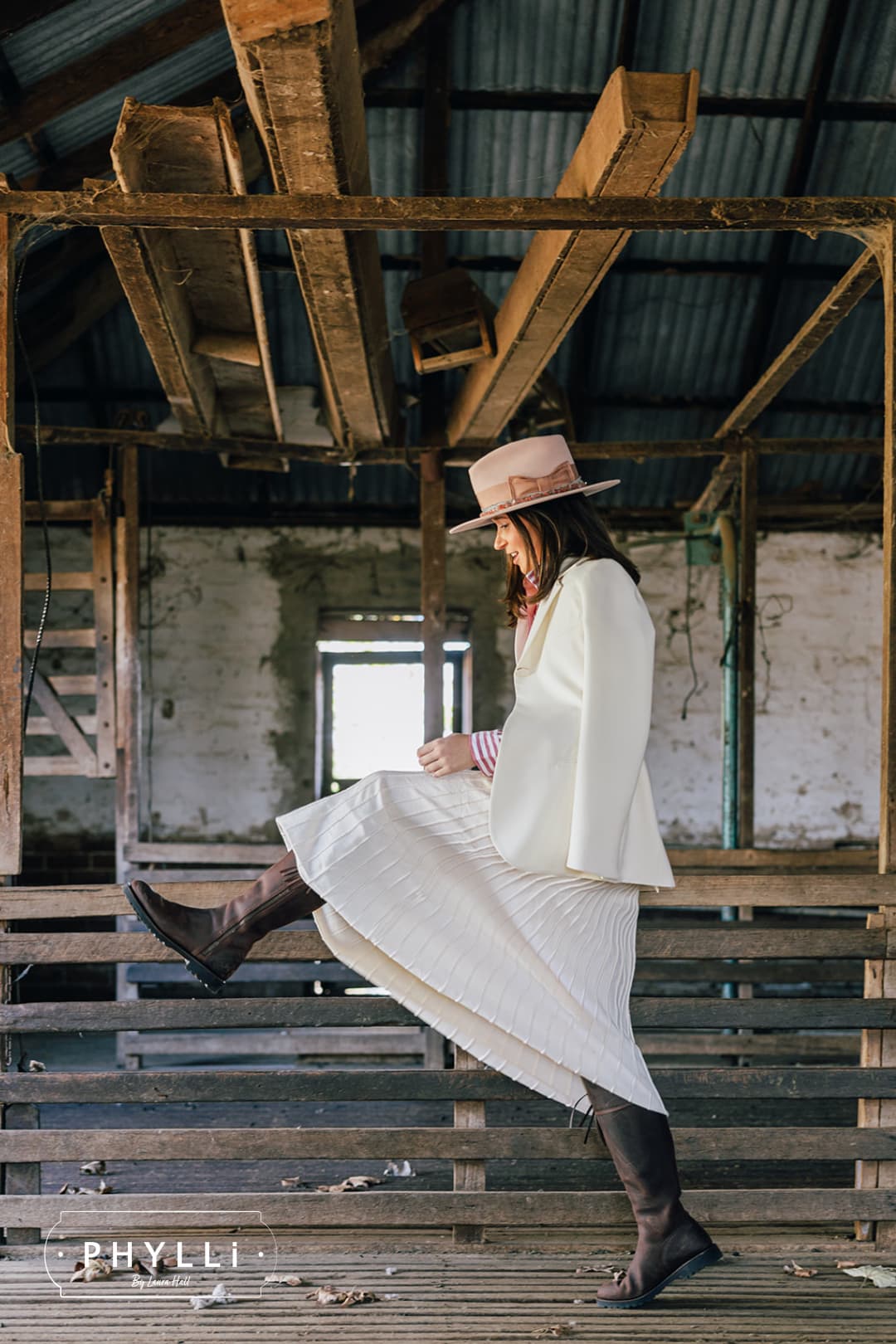Brunette model wearing the Tourmaline Baby Pink felt hat by PHYLLi Designs with dirty rose grosgrain bow while walking through a rustic shearing shed.