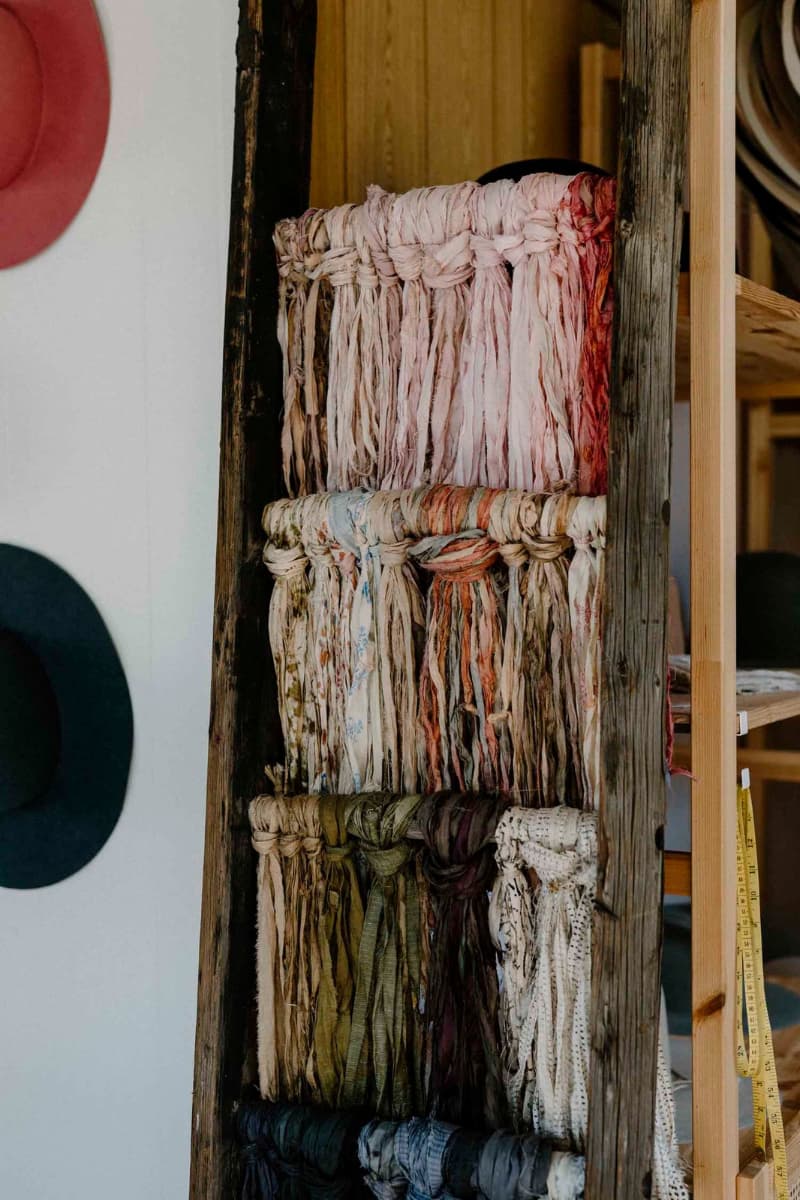 Assorted sari silk hat trimmings hanging on wooden ladder in the PHYLLi hat studio.