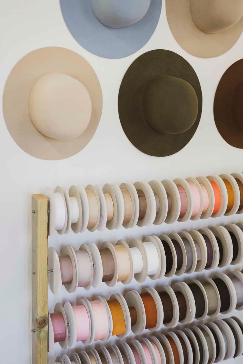Hat bases and grosgrain ribbon spools displayed on studio wall in the PHYLLi hat studio.