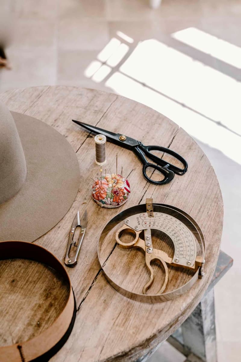 Hatmaking tools, thread spool, scissors and felt hat base on wooden workbench in the PHYLLi hat studio.