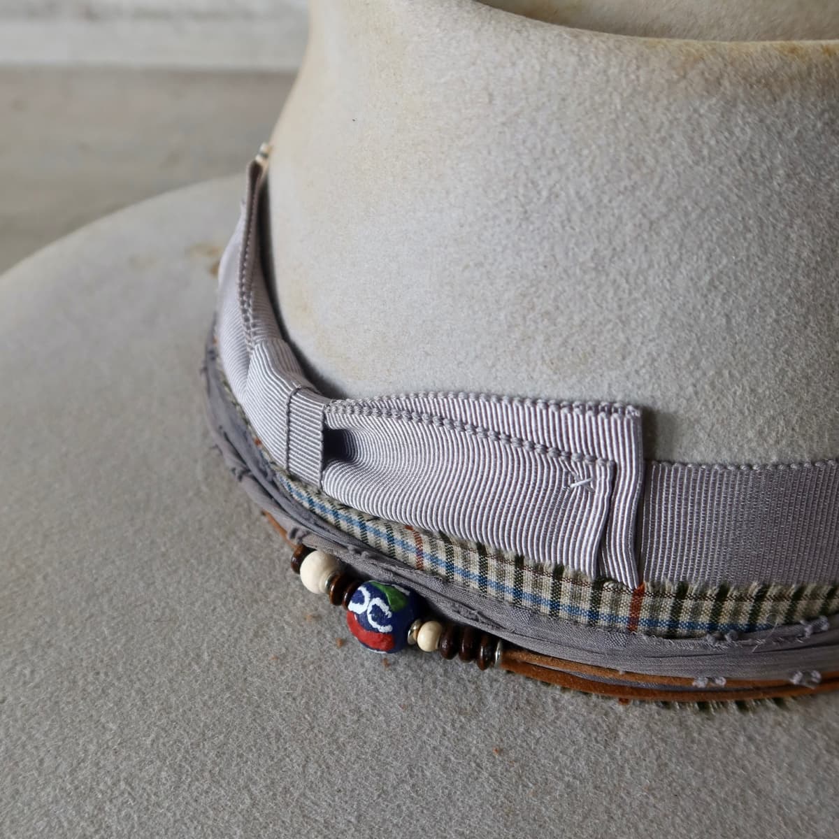 Close up detail of the Watson Limited Edition felt hat showing wooden beads and hand painted recycled glass beading on tan suede string.