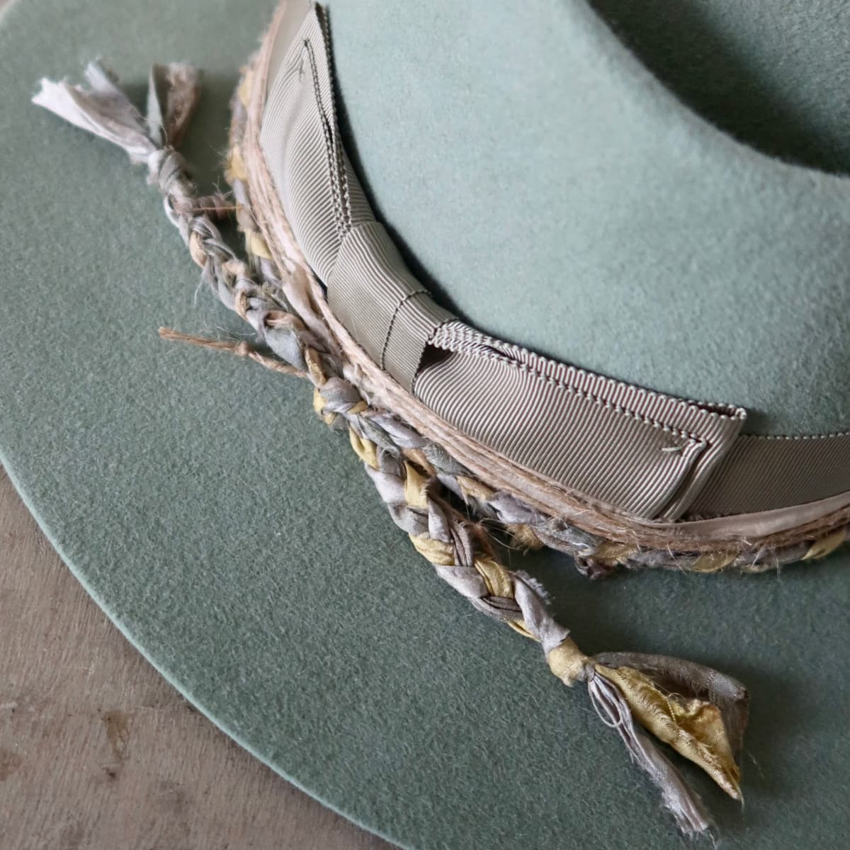 Close up detail of the Wheatley Limited Edition felt hat showing plaited sari silk trim in blues and greens with twine wraps.