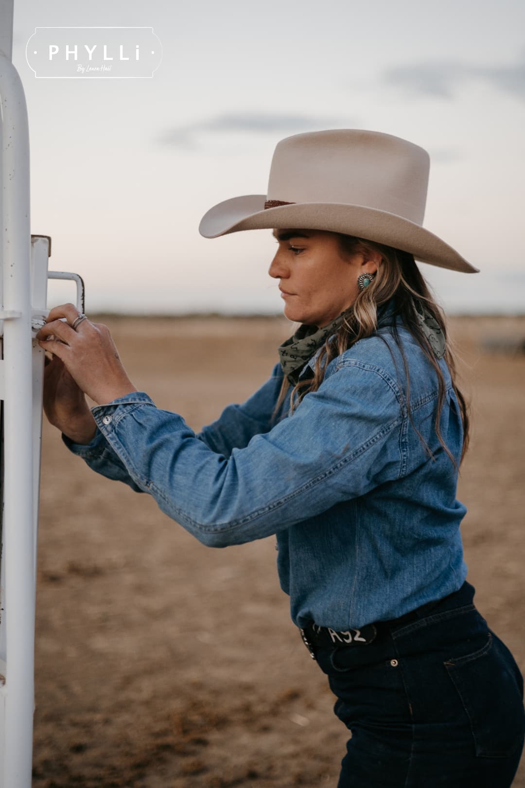 Model wearing the beige cowboy hat Wheeler Beige by PHYLLi Designs with 12 strand chocolate leather hat band while securing a horse float gate.