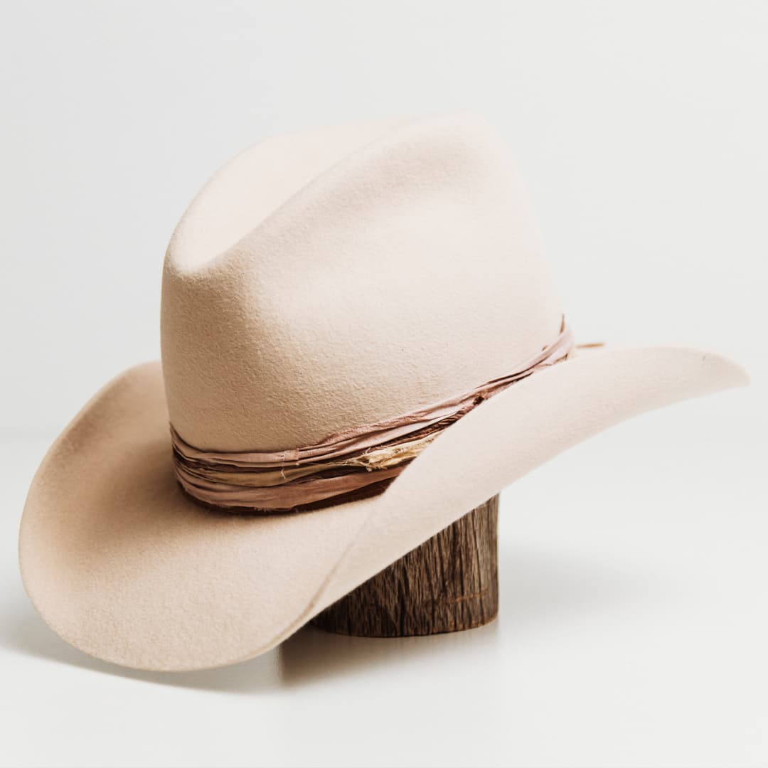 Front left angle of the Wrapped Wheeler beige felt hat by PHYLLi Designs with dusty pink and nude tie dye sari silk wrapped band.