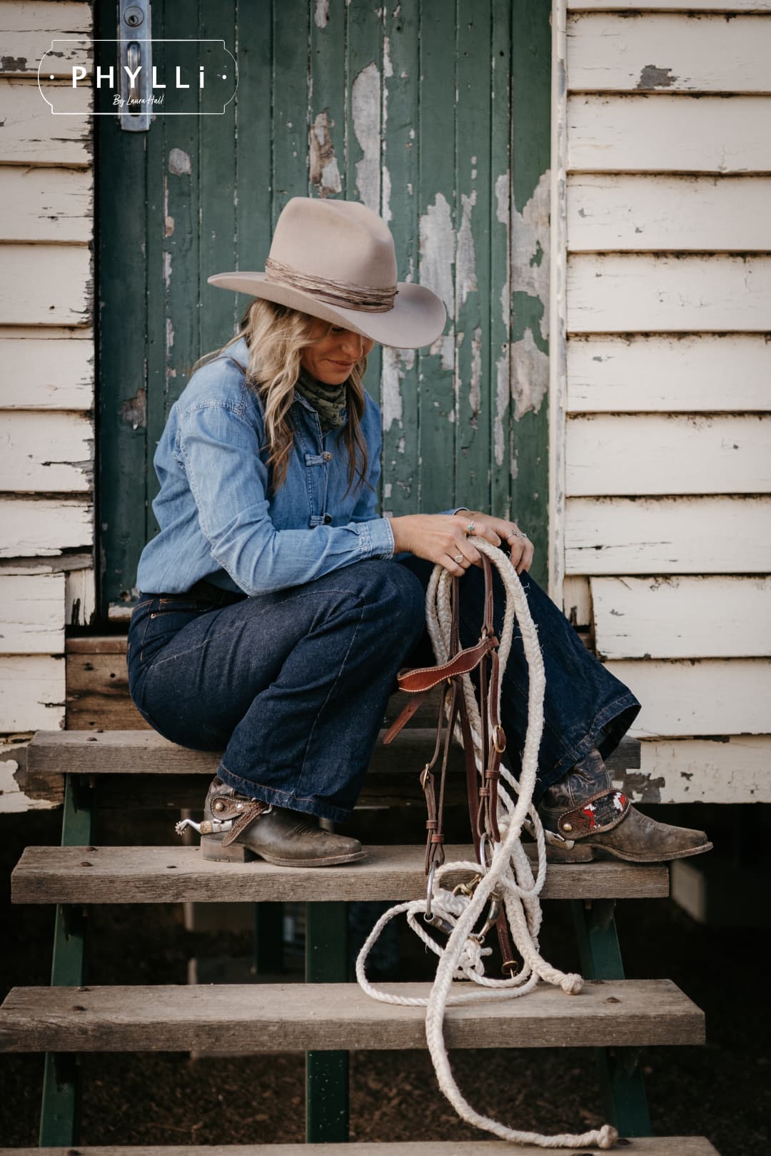 Woman wearing the Sahara cowboy hat Wrapped Wheeler Sahara by PHYLLi Designs with tonal tie-dye sari silk wrap sitting on wooden steps holding a stockman rope.