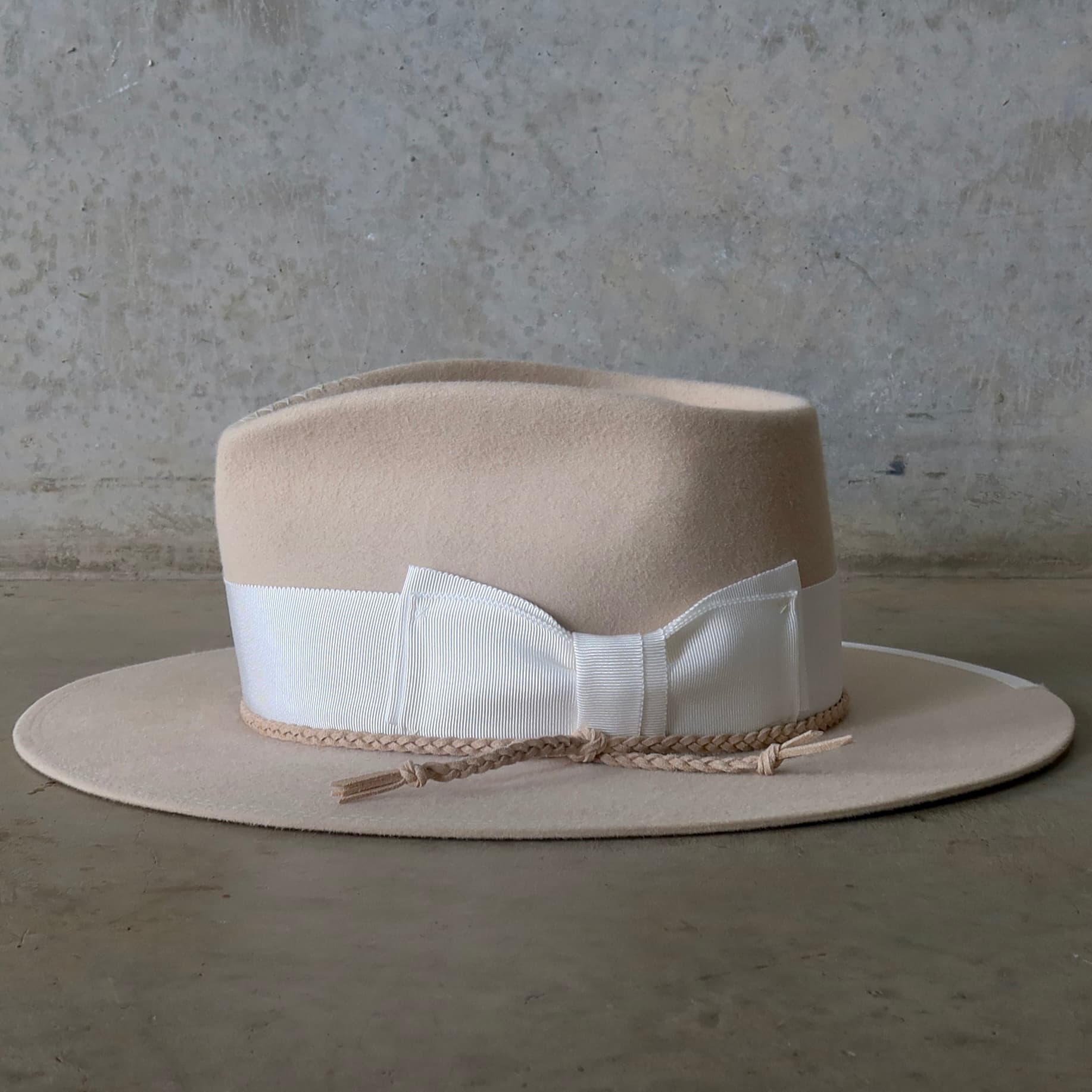 Left side view of the beige felt hat Yolande by PHYLLi Designs with ivory Japanese grosgrain bow band and ivory brim trim.