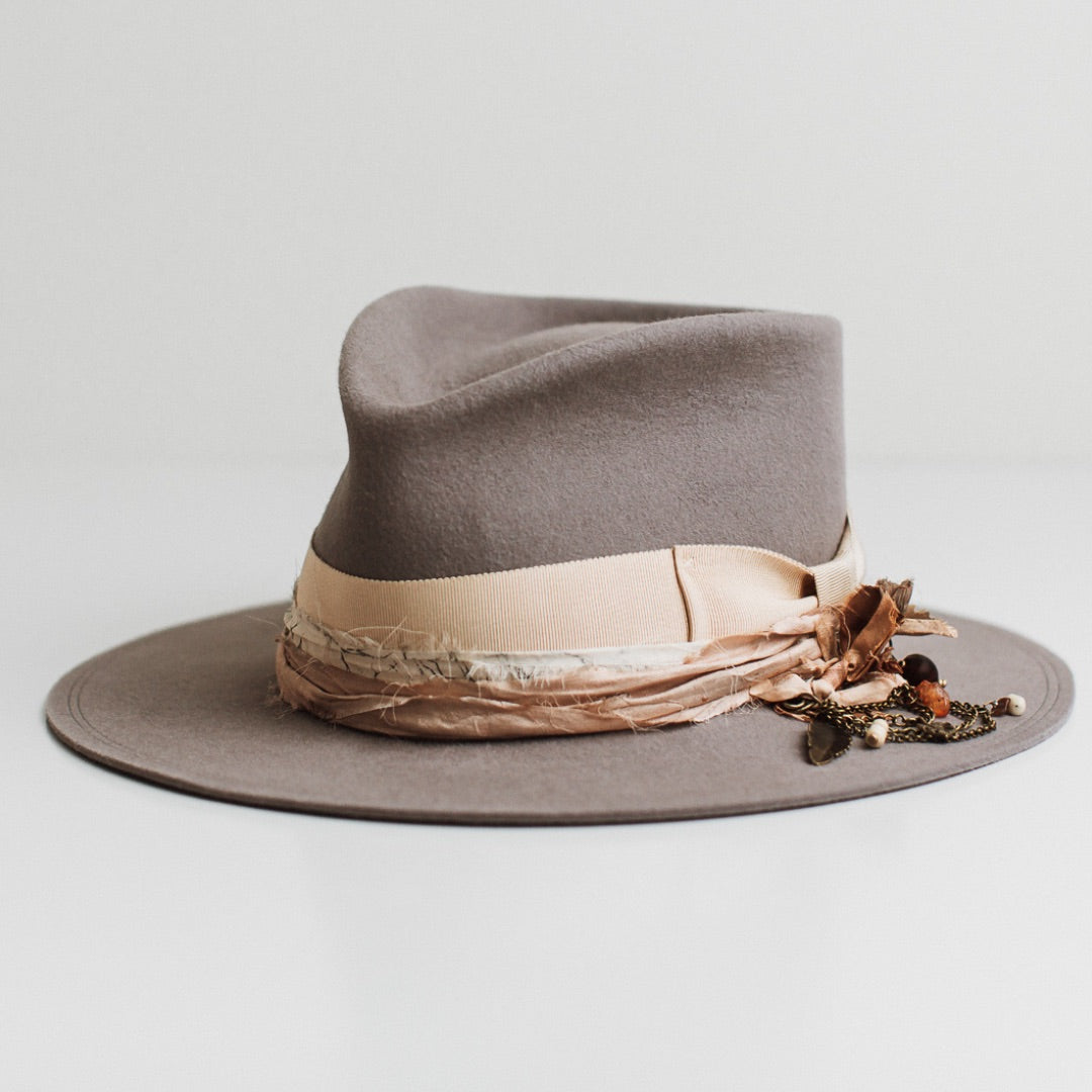 Front left angle of the Arrowtown taupe felt hat by PHYLLi Designs with sand grosgrain bow band and apricot and black white sari silk trimming.