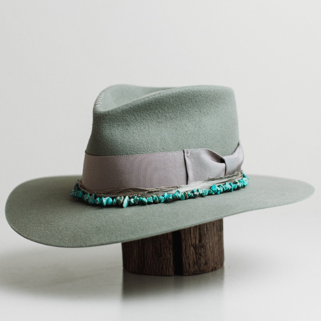 Front left angle of the Aurora sage felt hat by PHYLLi Designs with dove grosgrain bow band and turquoise stone hat necklace.