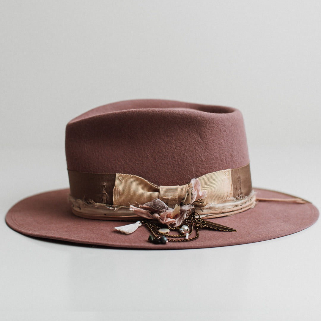 Left side view of the Celia blush felt hat by PHYLLi Designs with taupe grosgrain brim trim, suede string in nude and black and white sari silk trimming.