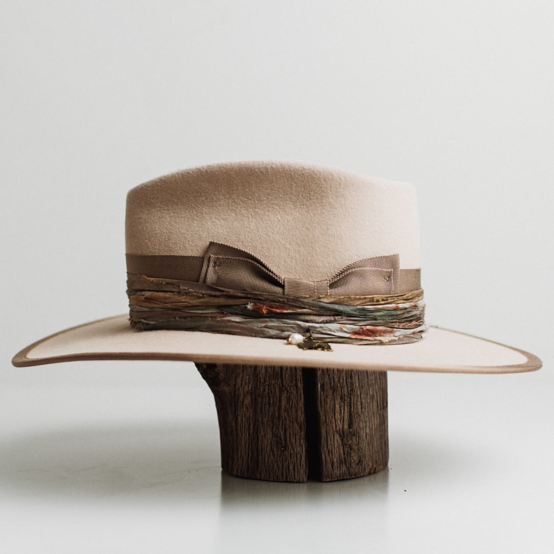 Left side view of the Cunningham beige felt hat by PHYLLi Designs with sari silk trim in speckled blue and rust tones and bronze charm cluster.