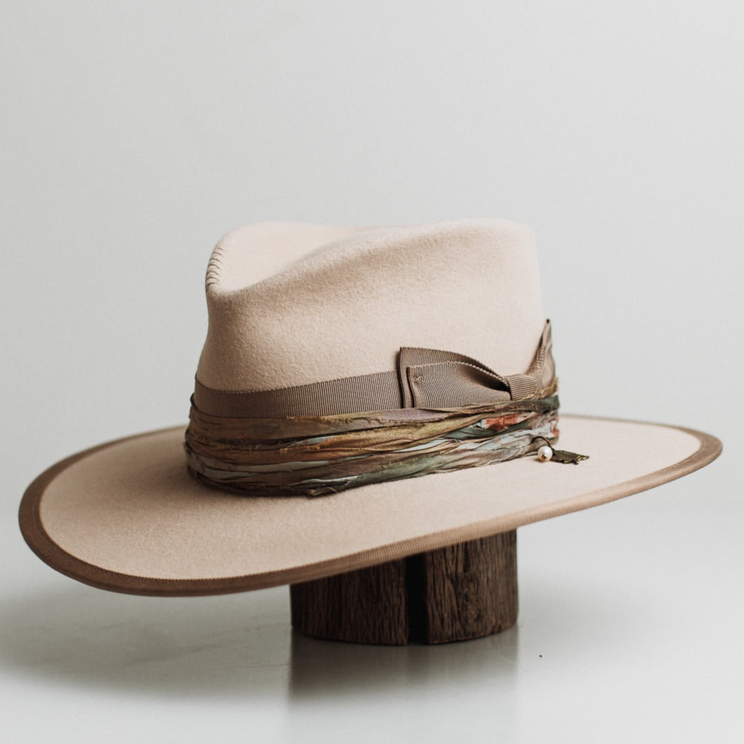 Front left angle of the Cunningham beige felt hat by PHYLLi Designs with taupe grosgrain band and jewel toned sari silk trimming.