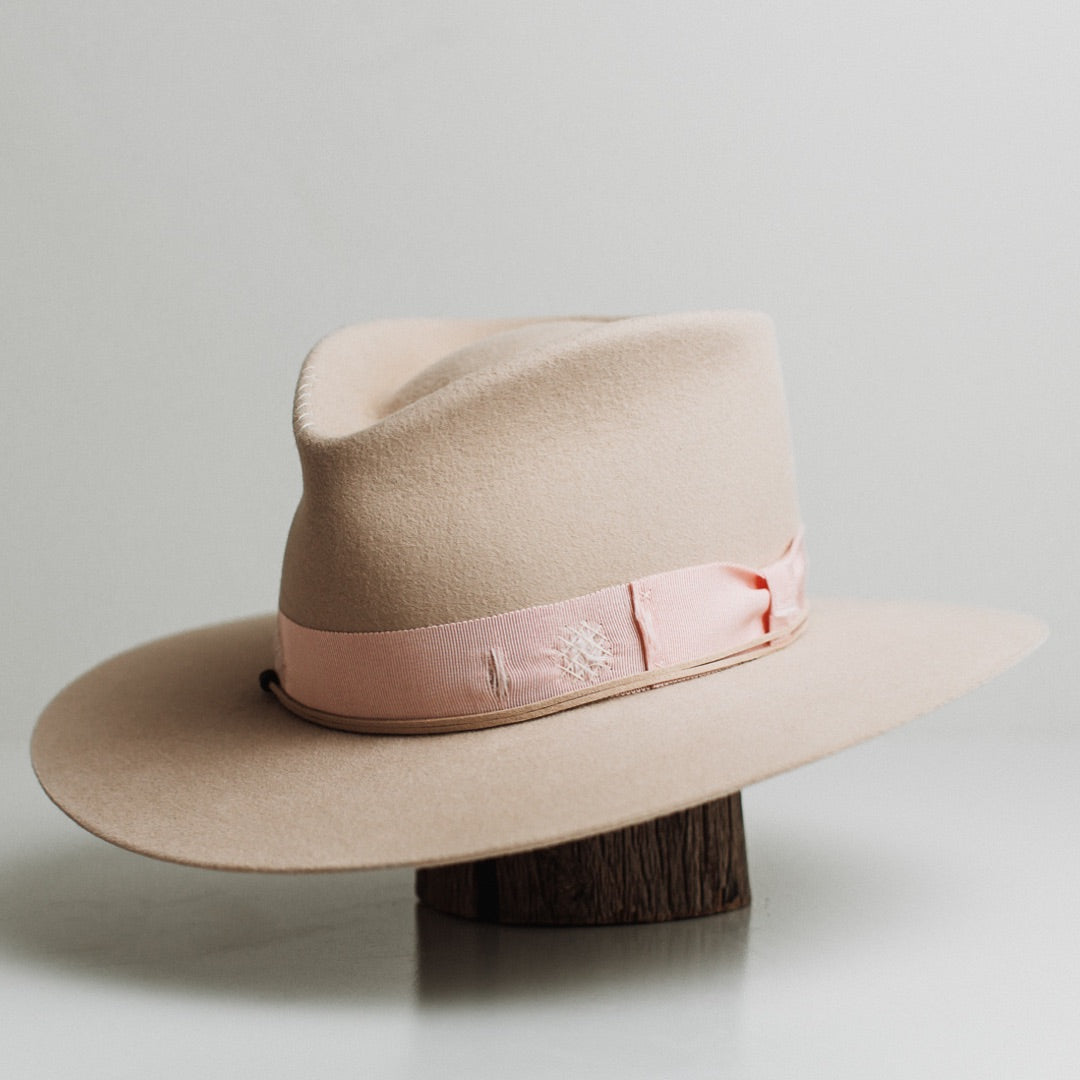 Front left angle of the Curlewis beige felt hat by PHYLLi Designs with distressed sherbet pink grosgrain band and nude suede string.