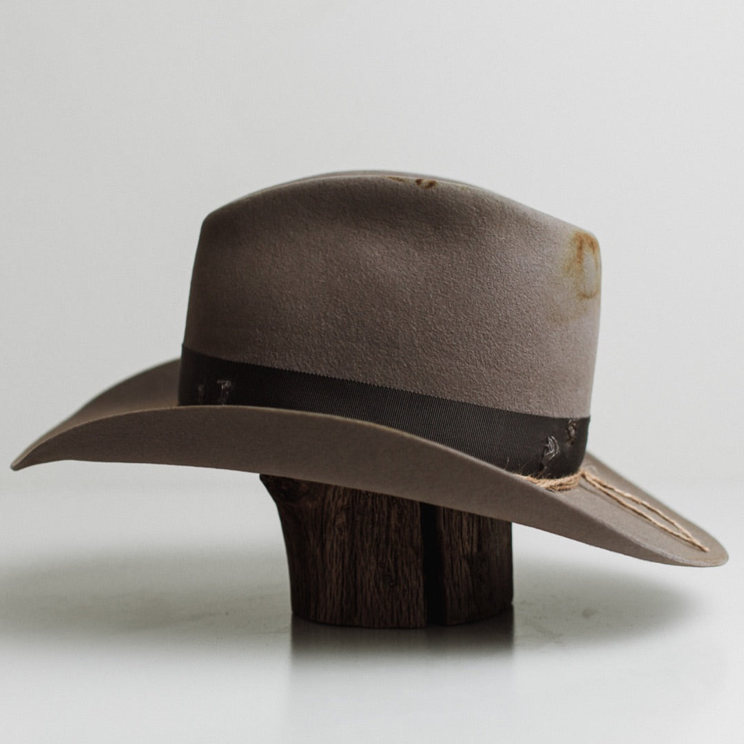 Left side view of the Finse cement felt cowboy hat by PHYLLi Designs with distressed steel grey grosgrain band and three twine wraps finished with turquoise beads.