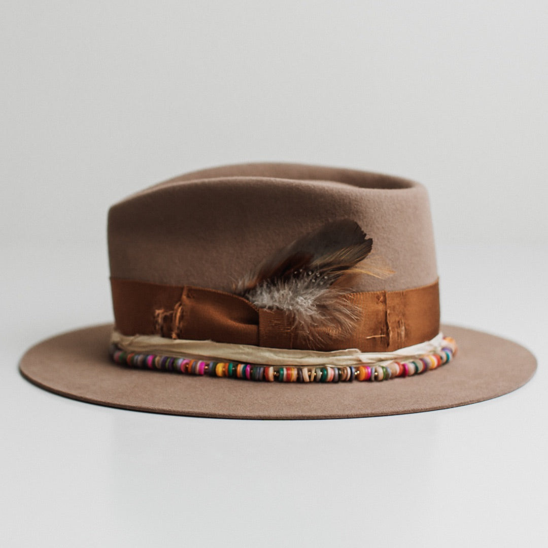 Left side view of the Mango Sahara felt hat by PHYLLi Designs with rainbow disc hat necklace and cream sari silk trimming.