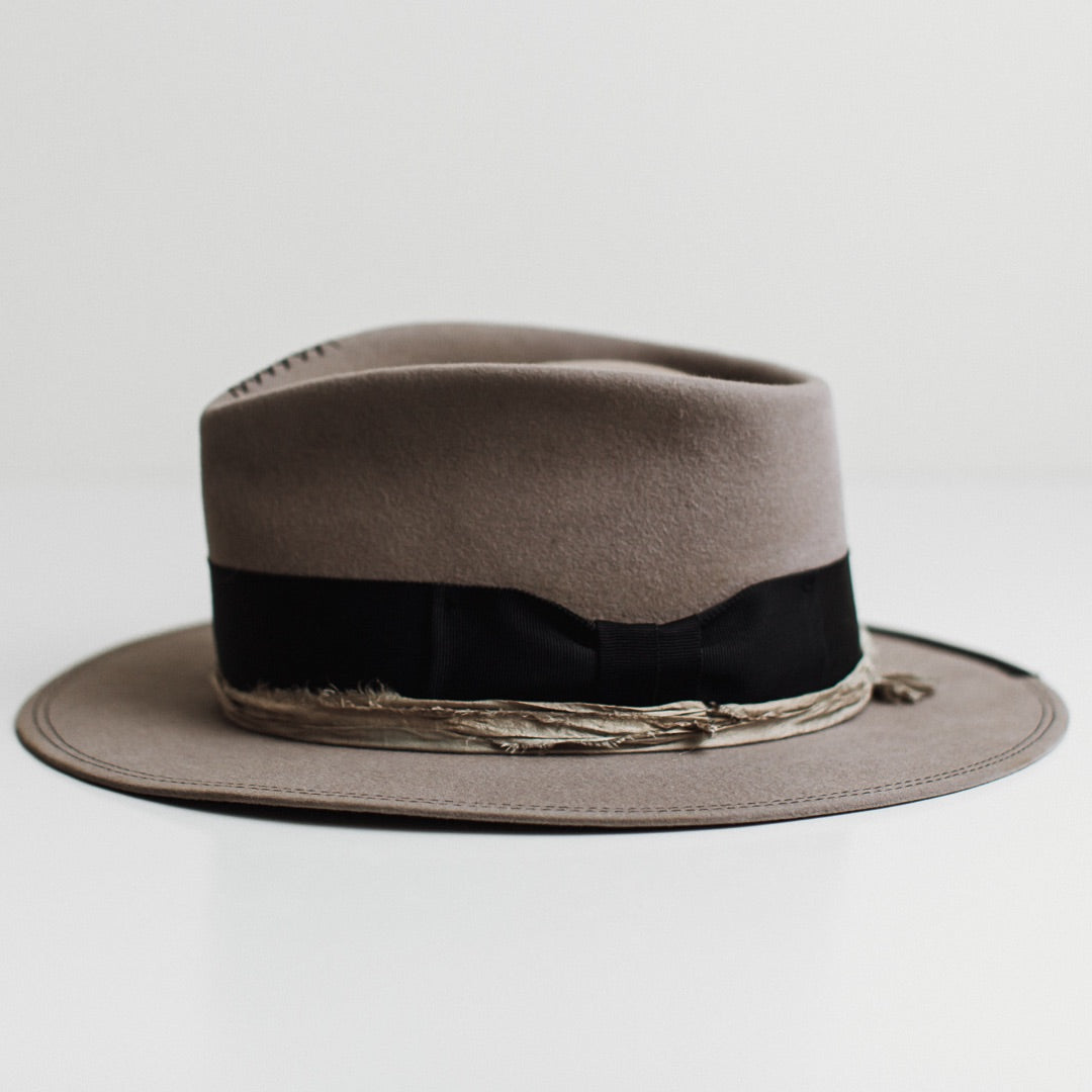 Left side view of the Specter taupe distressed felt hat by PHYLLi Designs with dark navy grosgrain 1/3 brim trim and smoke sari silk trimming.